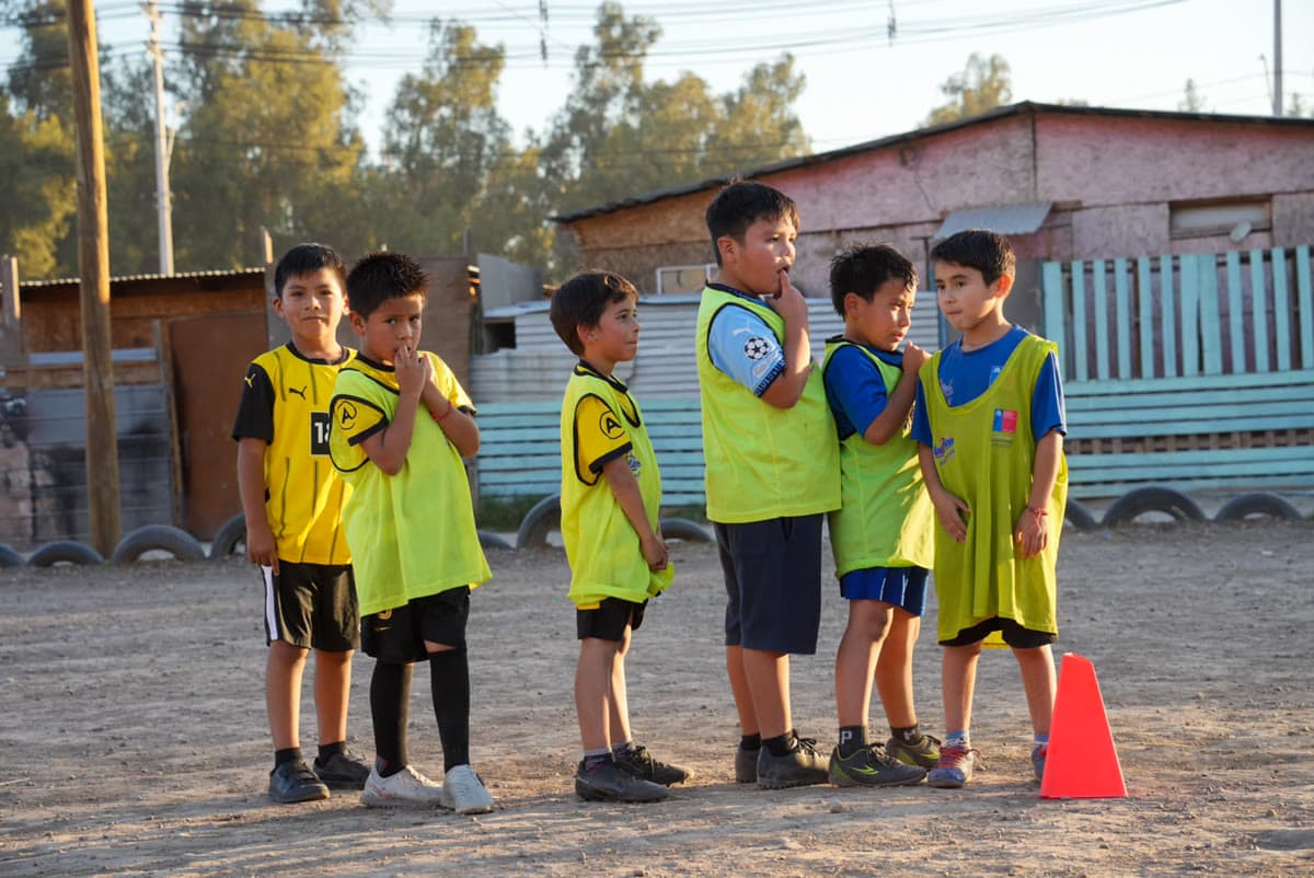 Grupo de niños con petos conversando con su entrenador antes de empezar el entrenamiento